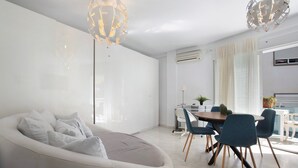 Un salon moderne avec un canapé blanc, une table à manger avec des chaises et une grande fenêtre avec des rideaux.