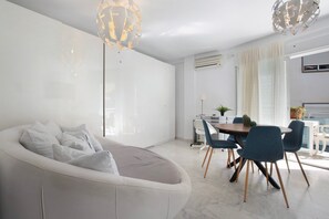 Ein modernes Wohnzimmer mit einem weißen Sofa, einem Esstisch mit Stühlen und einem großen Fenster mit Vorhängen.