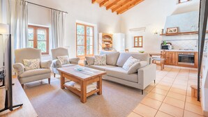 Una sala de estar con sofá, sillones, una mesa de centro y televisor. Cuenta con una zona de cocina con estufa, horno y alacenas.