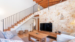 Una sala de estar con una escalera, un televisor y una pared de piedra.