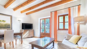 Un salon avec un plafond en bois, un téléviseur, une table à manger avec des chaises, un canapé et une fenêtre avec des rideaux.
