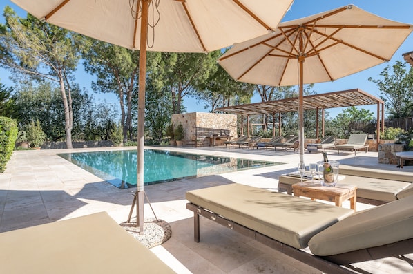 A poolside area with lounge chairs, umbrellas, and a stone structure.