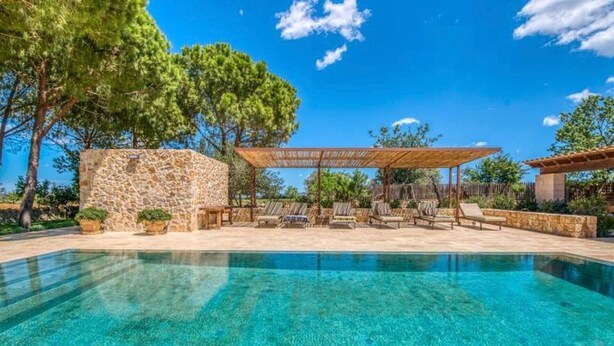 Une piscine aux eaux cristallines, bordée d’un mur en pierre et surmontée d’une pergola avec des sièges.