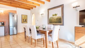 Un coin repas avec une table en bois, des chaises blanches, un réfrigérateur et un tableau accroché au mur.