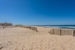 Ein sandiger Strand mit einer Holzlattenveranda und einem Gebäude im Hintergrund.