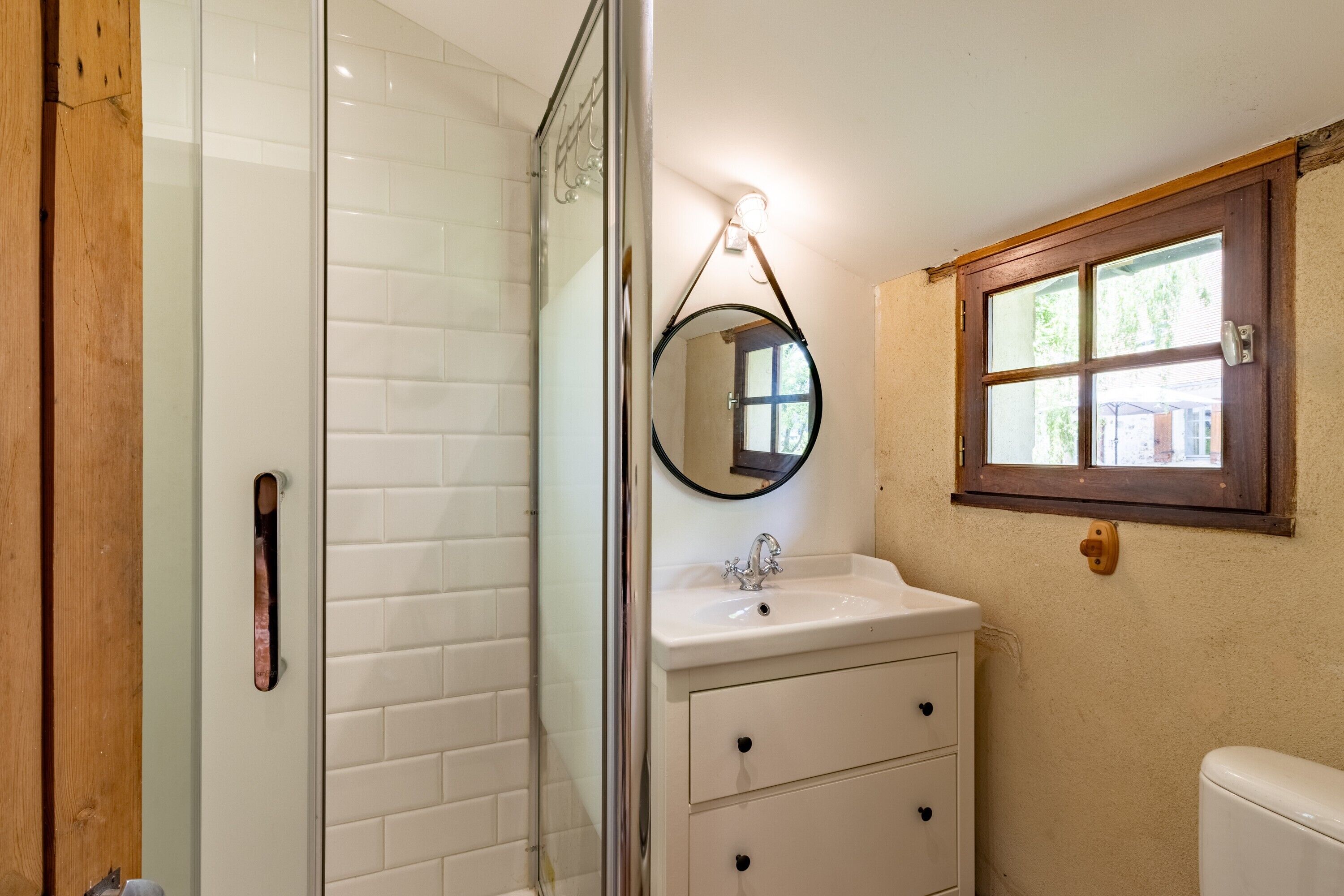 A bathroom with a glass shower enclosure, a sink with a mirror, and a window.