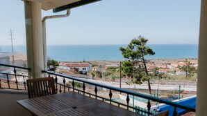 Een balkon met een houten tafel en stoelen, uitkijkend op een kustgebied met gebouwen en een heldere lucht.