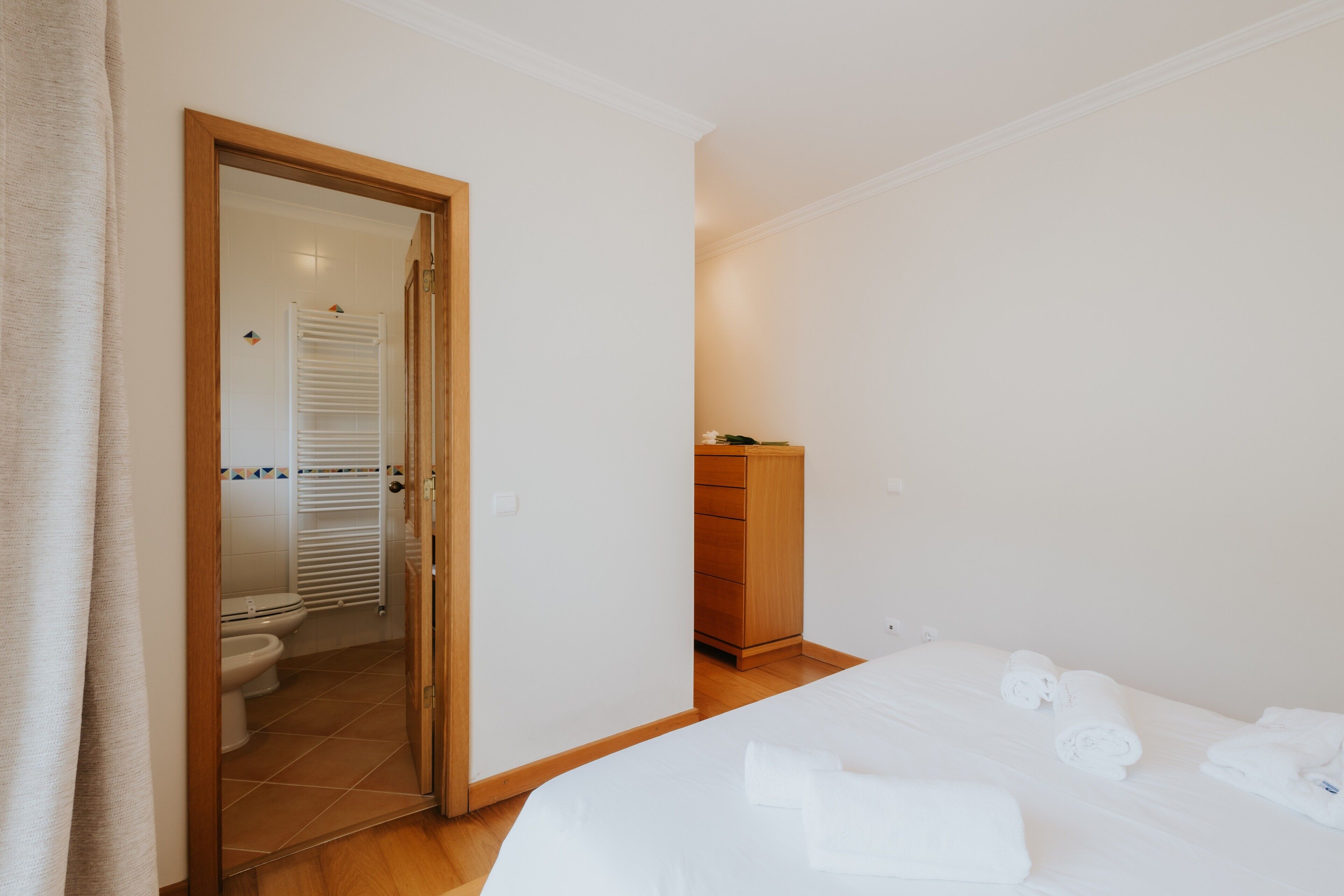 A bedroom with a bed, a wooden dresser, and a bathroom with a toilet and shower.