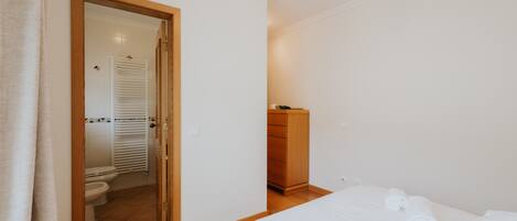 A bedroom with a bed, a wooden dresser, and a bathroom with a toilet and shower.