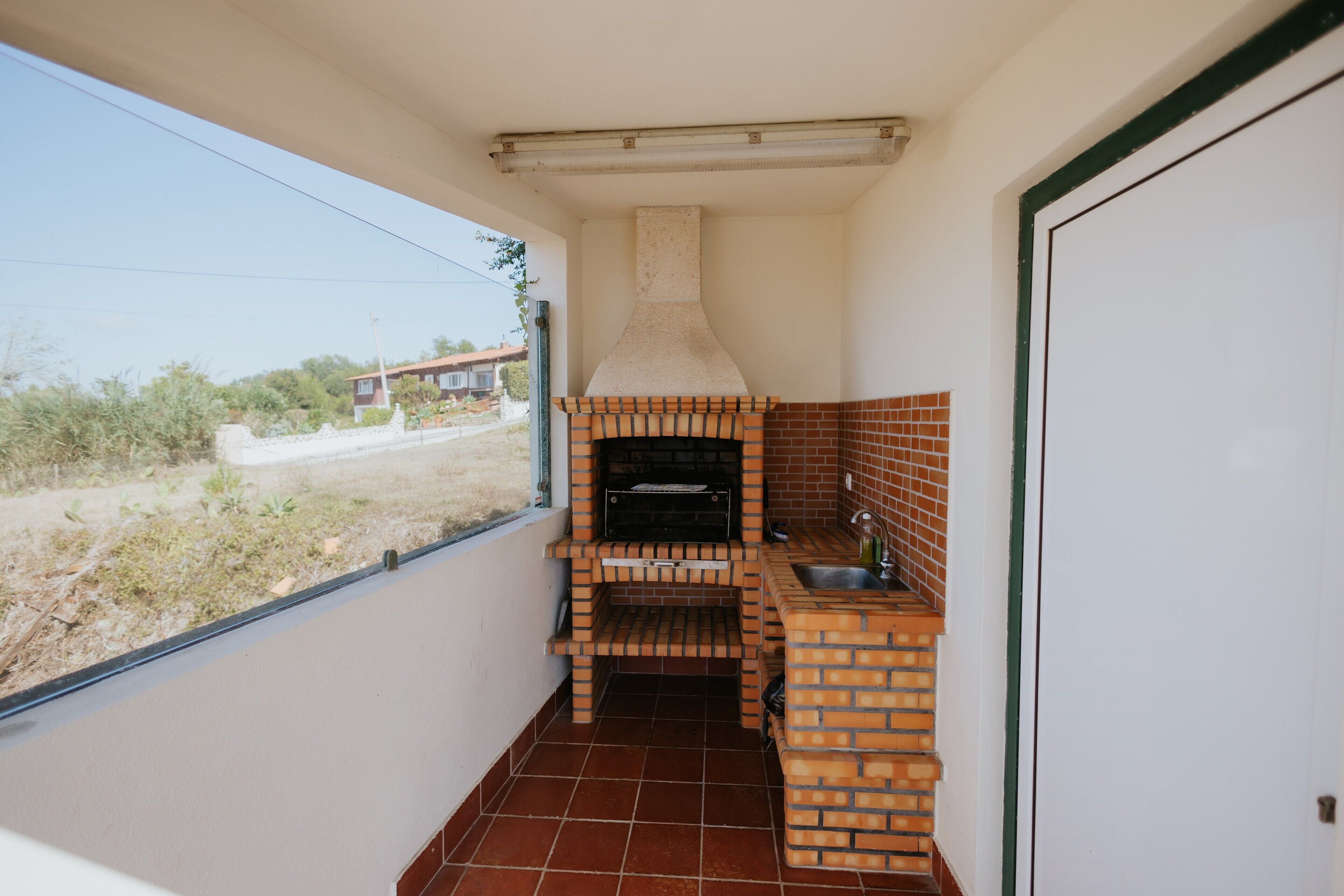 Un'area cucina esterna con forno in mattoni, lavello e finestra che si affaccia su un quartiere residenziale.