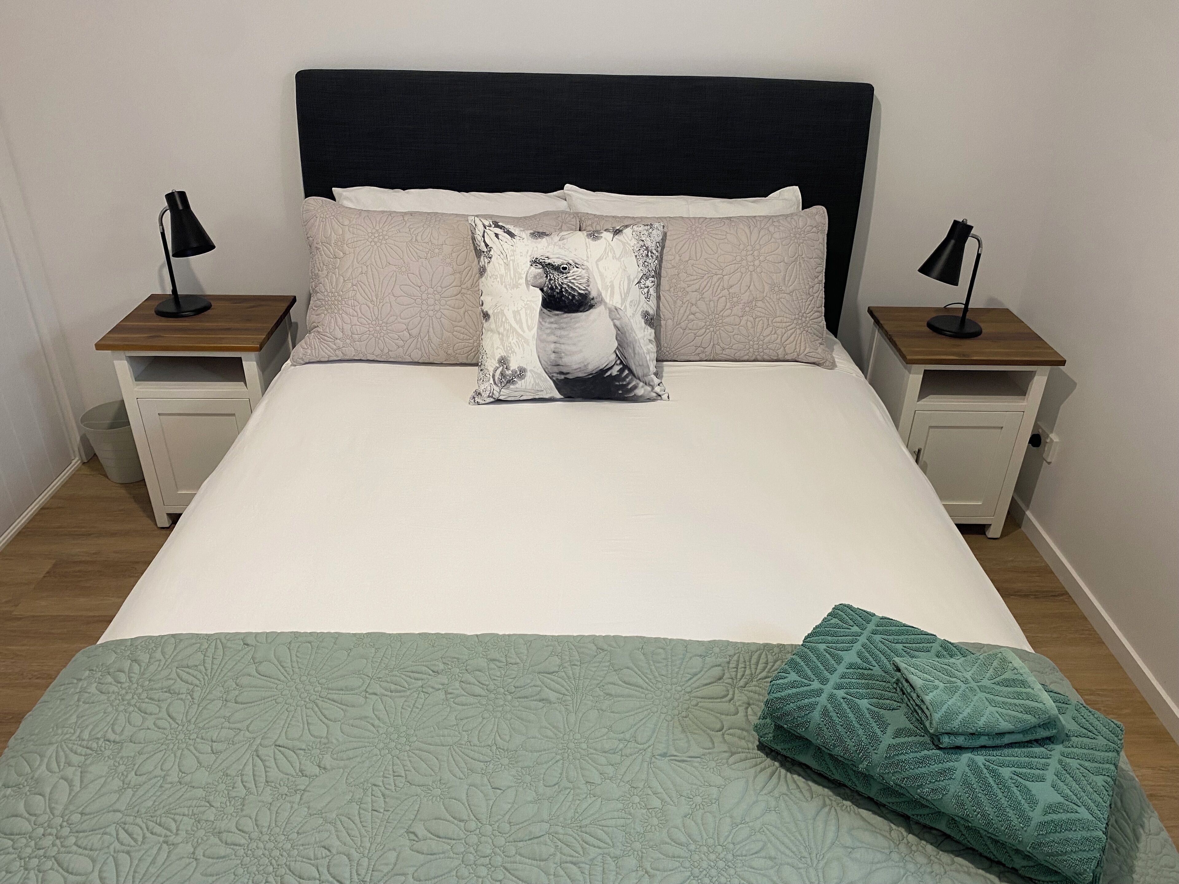 A neatly made bed with a floral bedspread, a decorative pillow, and a folded blanket on the side. There are two bedside tables with lamps and a small trash bin.