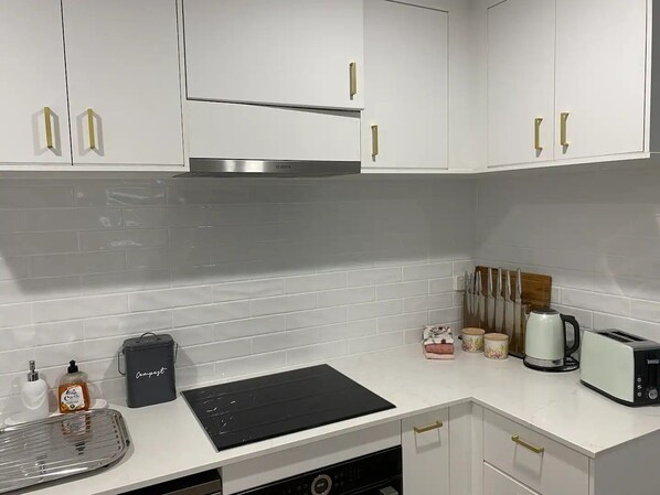 A modern kitchen with white cabinets, a Bosch range hood, a black induction cooktop, a dishwasher, and a toaster.