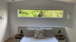 A bedroom with a large window, a bed with multiple pillows, two bedside tables with lamps, and a wooden floor. - Fantastic views, comfortable beds. Close to Banya Bathhouse Spa & Crystal Castle (Mullumbimby)