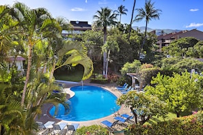 A pool surrounded by palm trees and lounge chairs, with a view of a mountain range in the background. - Tropical 2BR Retreat with Dual Master Suites (Kihei)