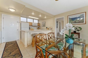 A modern kitchen with white cabinets, a microwave, and a dining area with a glass table and wooden chairs. - Tropical 2BR Retreat with Dual Master Suites (Kihei)