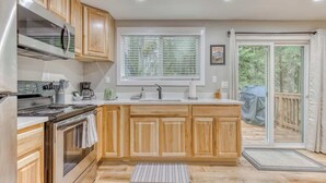 Une cuisine moderne avec des meubles en bois, un réfrigérateur en acier inoxydable, un four encastré et une grande fenêtre équipée de stores.