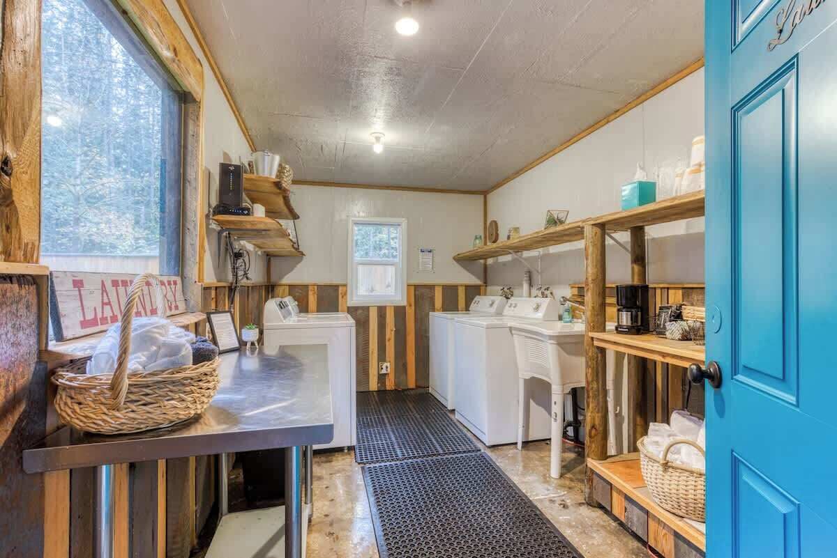 A laundry room with wooden walls, a washing machine, a dryer, and shelves with various items.
