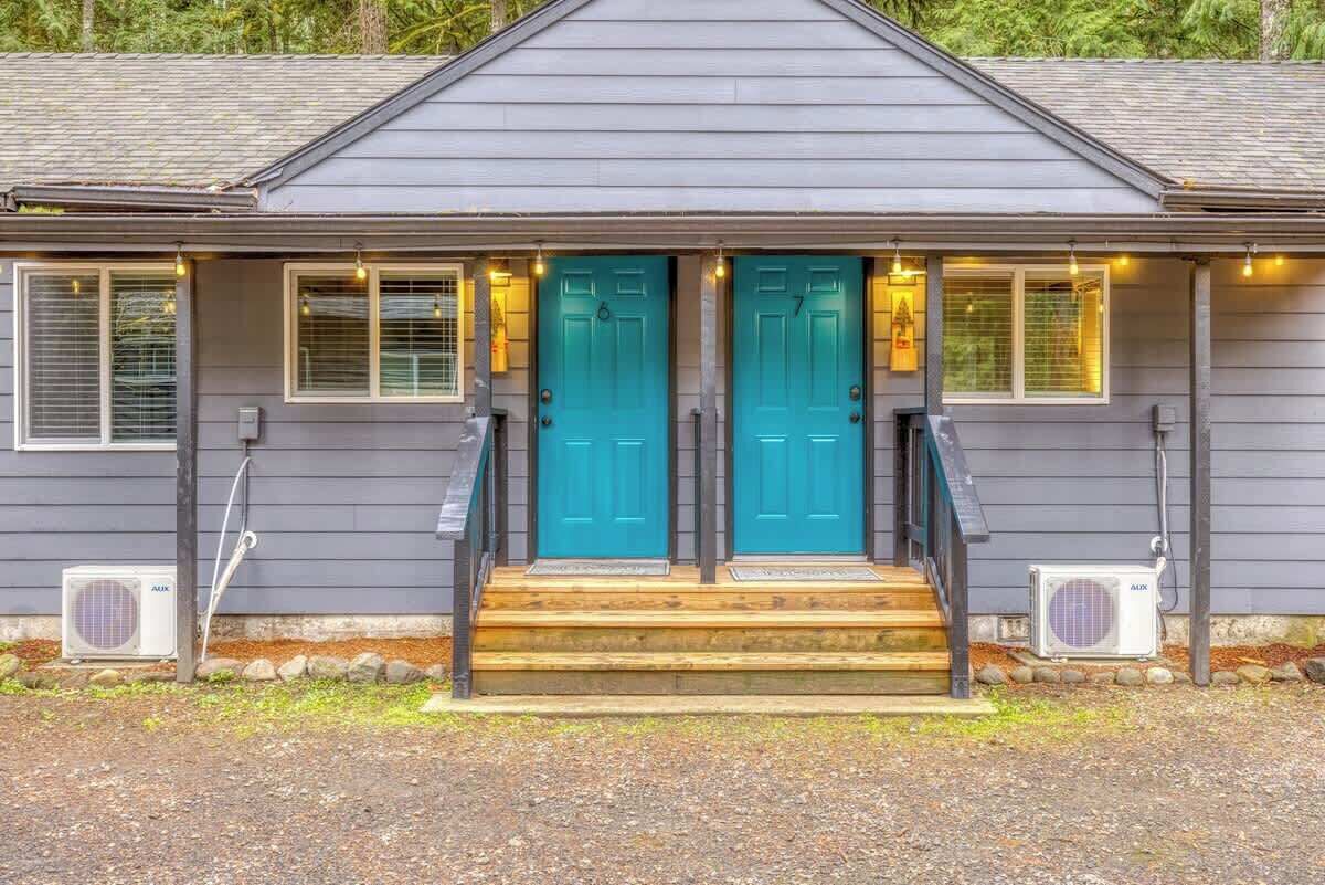 Une maison avec deux portes bleues, un porche avant en bois et deux unités de climatisation.