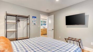 Un dormitorio con cama, televisor montado en la pared, armario y puerta que da a una cocina.
