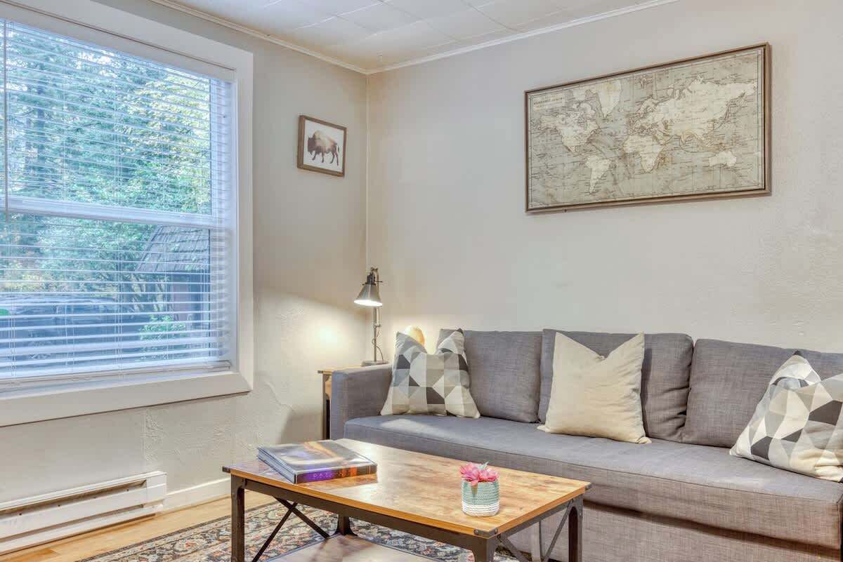 Una sala de estar con un sofá gris, una mesa de centro con libros, una lámpara y un mapa mundial en la pared.
