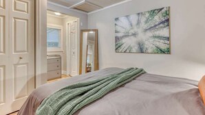 A bedroom with a bed, a green knitted throw, a painting, and a door leading to another room.