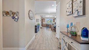 A hallway with a wooden floor, a rug, a coat rack with house-shaped hooks, and a mirror on the wall.