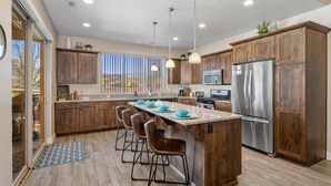 A modern kitchen with wooden cabinets, a stainless steel refrigerator, and a large island with bar stools.