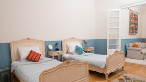 A room with two beds, a small table, a lamp, a sofa, and a patterned rug.