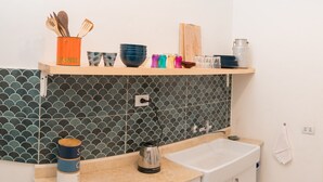 A kitchen with a tiled backsplash, a wooden shelf with kitchenware, a sink, and a countertop.