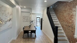 A modern kitchen with white cabinets, a dining area with a wooden table, and a brick wall.
