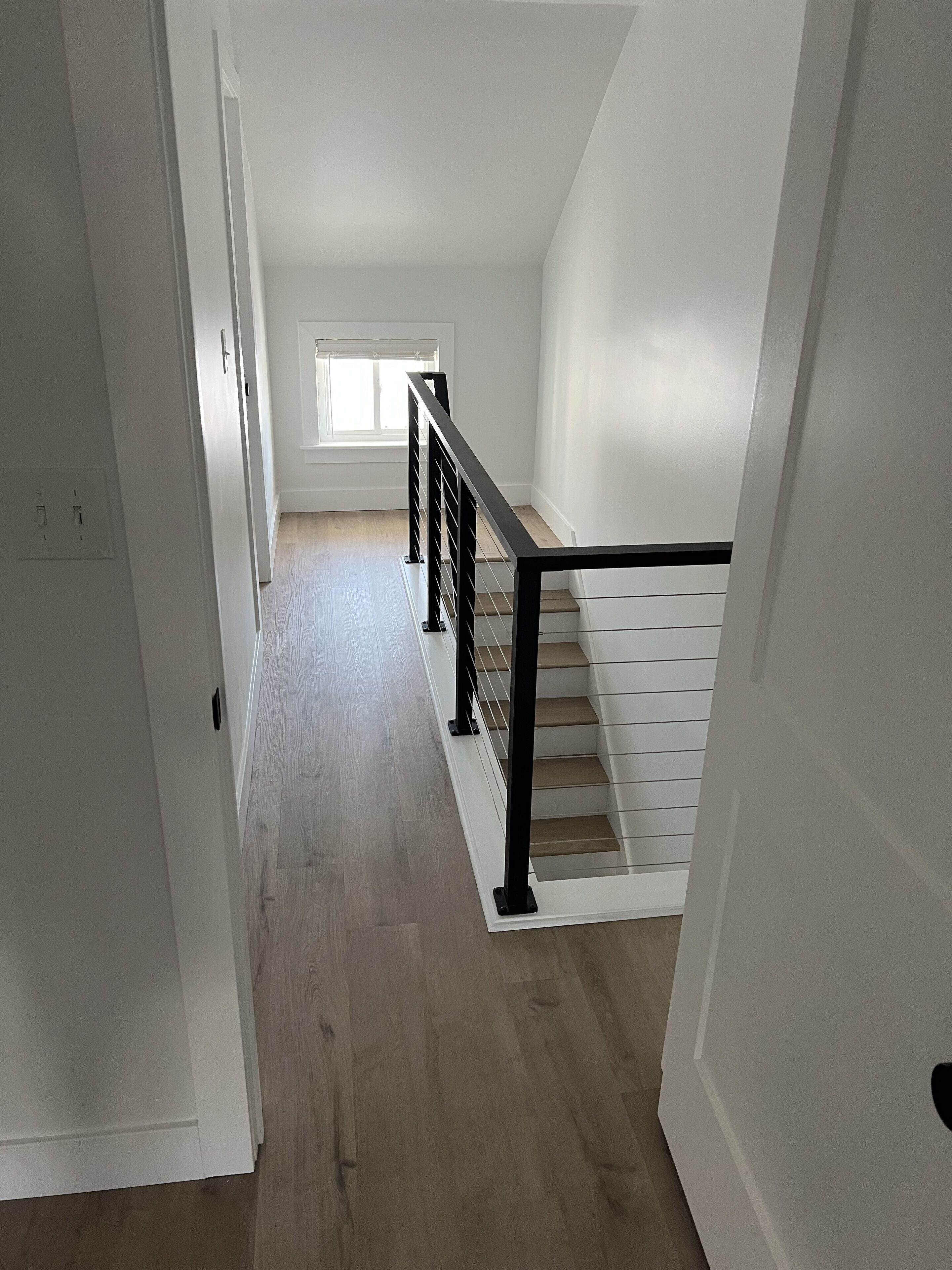 A staircase with a black railing, white walls, and a wooden floor.
