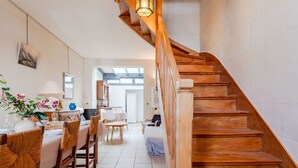 Un escalier en bois mène à un coin repas où se trouvent des chaises en osier et une table dressée pour le repas.