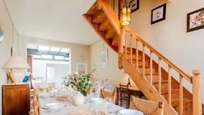 Un coin repas agrémenté d’un escalier en bois, d’une table dressée pour quatre personnes et d’un vase de fleurs.