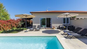 A poolside area with lounge chairs, umbrellas, and a building with a tiled roof. - Vacation home Eja by Interhome (Buje/Plovanija)