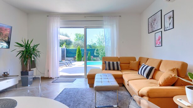 A modern living room with a sofa, a coffee table, and a TV. There is a sliding glass door leading to a pool area. - Vacation home Eja by Interhome (Buje/Plovanija)