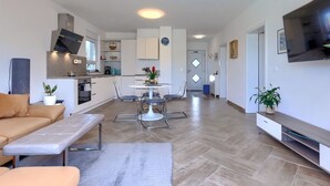 A modern living room with a sofa, a dining table with chairs, a kitchen area with cabinets and a TV. - Vacation home Eja by Interhome (Buje/Plovanija)