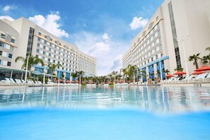 Un hôtel doté d’une grande piscine, de palmiers et de chaises longues.