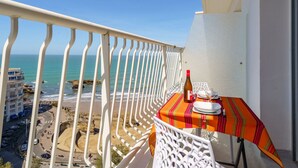 Un balcon avec une table dressée pour deux personnes, donnant sur une plage et l’océan.