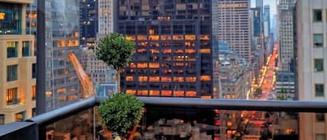 A table with a bottle of champagne, two glasses, and a candle, set against a cityscape with tall buildings and a flag.