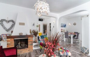 Cozy living space with a central fireplace, vibrant chair, and decorative wall piece, featuring a dining area and contemporary chandelier.