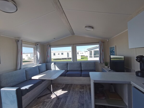 A compact living space with a sofa, a small table, a television, and a coffee machine.