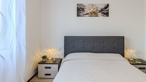 A bedroom with a large bed, two bedside tables, a wall-mounted artwork, and a window with curtains. - Lovely apartment for 4 people with WIFI, TV, balcony and panoramic view (Dorio)