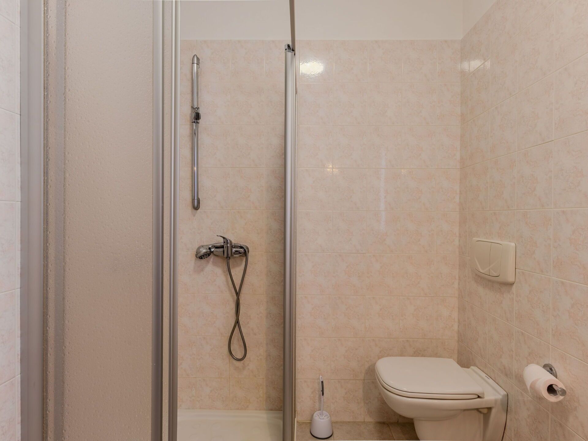 A bathroom with a glass-enclosed shower, a toilet, and a hand dryer.