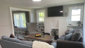 Una sala de estar con un sofá gris, una mesa de centro con fruta, una chimenea y un televisor montado encima.