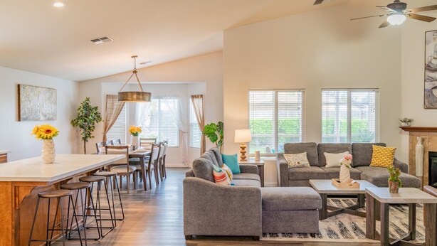 Ein geräumiges Wohnzimmer mit grauem Sofa, einer Essecke mit Holztisch und Barhocker sowie einem Kamin.