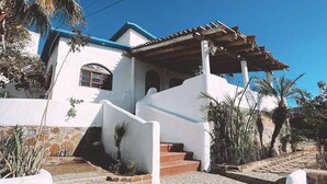 A white building with a blue roof, a staircase leading to the entrance, and a covered porch area. - Casa Núuk (Todos Santos)