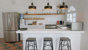 A modern kitchen with a stainless steel refrigerator, a microwave, a stove, and three bar stools. - Casa Núuk (Todos Santos)