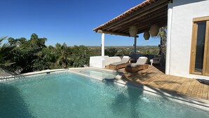 A swimming pool with lounge chairs and a pergola, surrounded by greenery and a clear sky. - Casa Núuk (Todos Santos)
