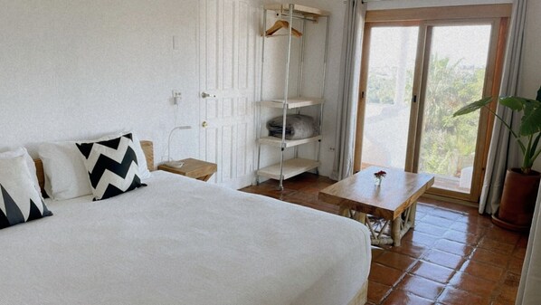 Un dormitorio con una cama grande, una mesa de madera, un estante colgante y una planta en maceta.