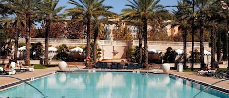 Una piscina rodeada de palmeras y sillas de descanso, con un edificio al fondo.
